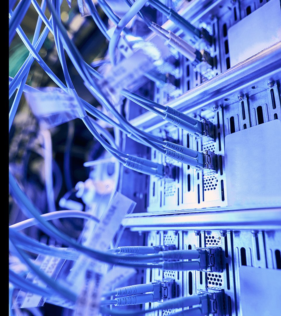 Cabos de rede conectados a equipamentos instalados em um rack técnico iluminado em tons azuis.