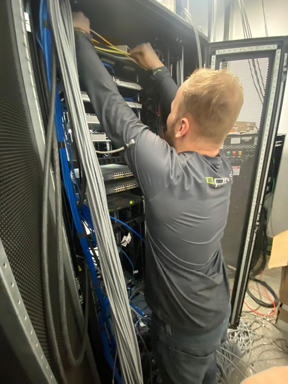 Profissional com uniforme da Optus trabalhando nas conexões de um rack